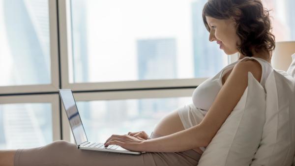 Žena sedí na posteli a vyhledává informace na počítači. Prohlášení o jménu dítěte.