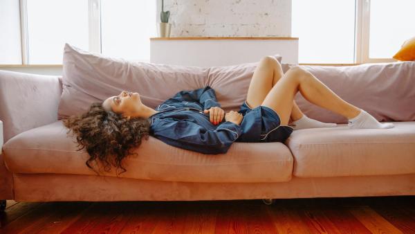 Žena leží na gauči s bolestmi břicha. Menstruace po porodu.