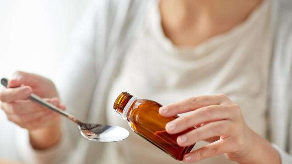 Žena se chystá nalít sirup na lžíci.