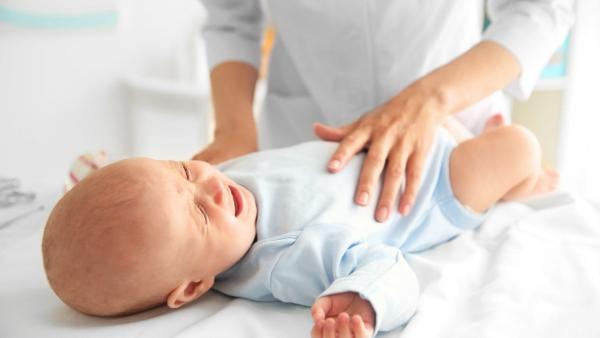 Miminko leží na podložce a maminka mu hladí bříško. Průjem a bolesti břicha u kojenců.