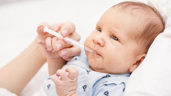 Maminka podává miminku vitamín D ve stříkačce.