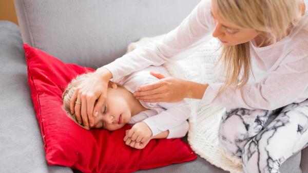 Holčička spinká na gauči a maminka ji hladí po vlasech. Zvracení u dětí.