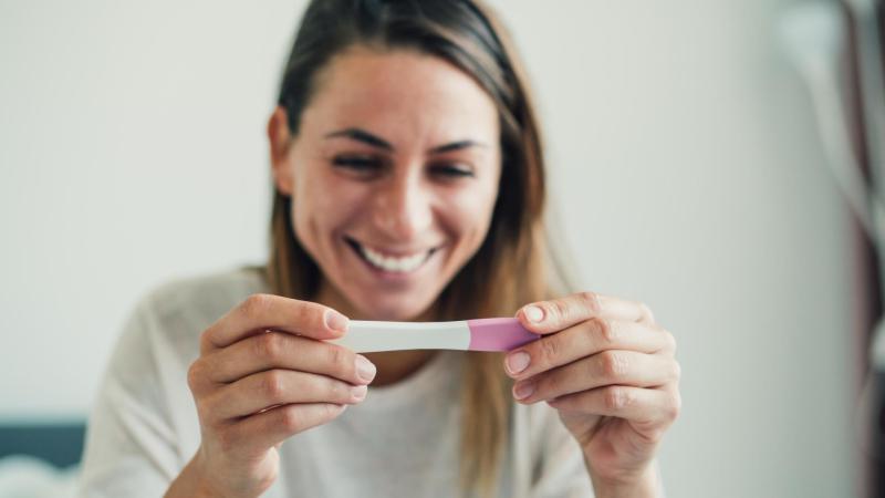 Žena se kouká na těhotenský test a raduje se z výsledku.