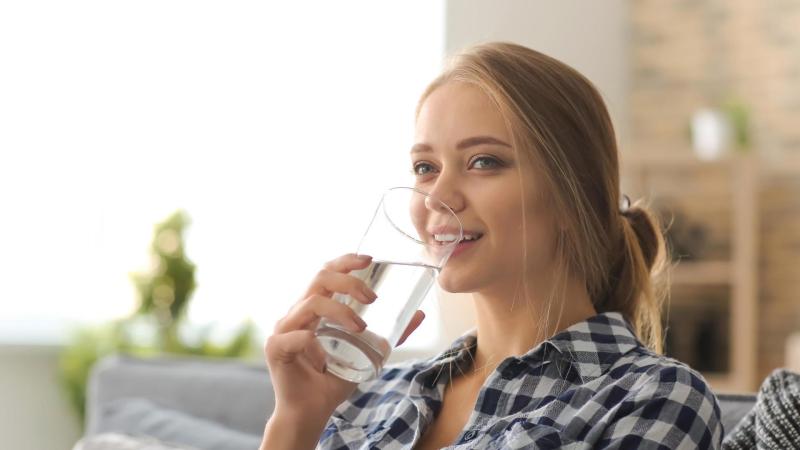 Žena sedí na gauči a pije čistou vodu.