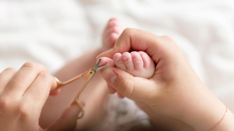 Maminka střihá nehty miminku s nůžkami s kulatou špičkou.