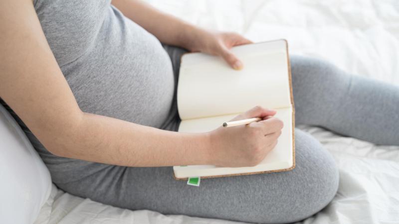 Těhotná žena sedí na gauči a sepisuje porodní plán.