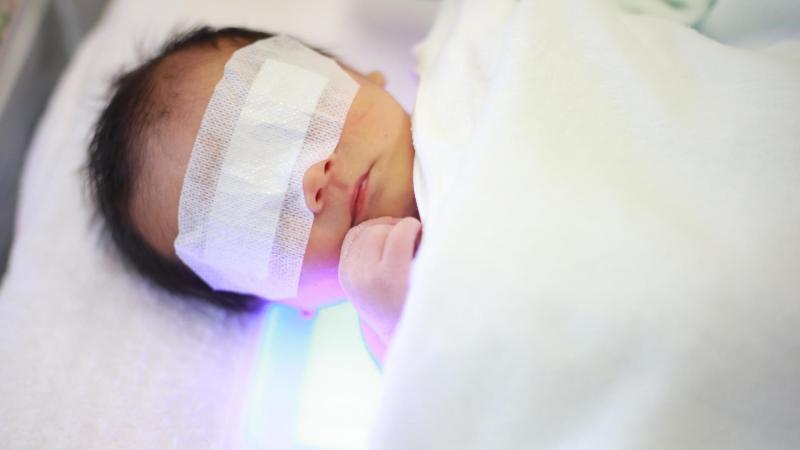 Miminko s novorozeneckou žloutenkou leží na posteli a svítí na něj modré světlo.