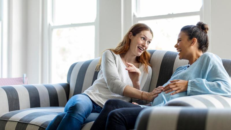 Těhotná žena s kamarádkou sedí na gauči a mluví o porodu.